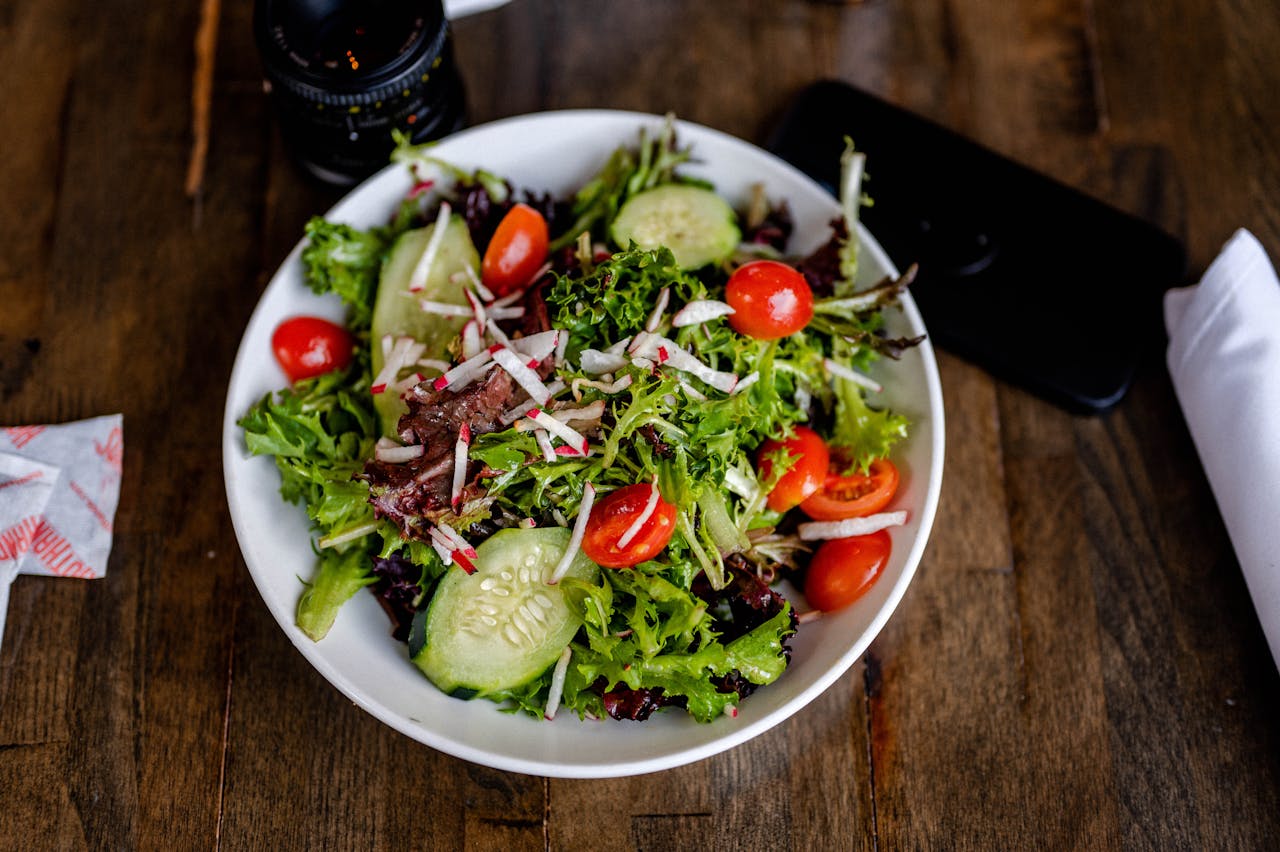 A vibrant fresh salad with greens, cherry tomatoes, cucumbers, and radishes on a wooden table for a healthy meal.
