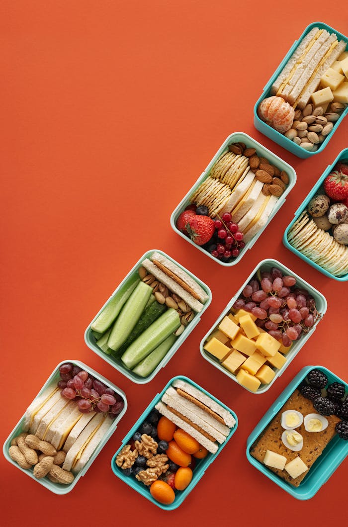 team-01 Flat lay of assorted healthy lunchboxes with fruits and nuts against vibrant orange background.